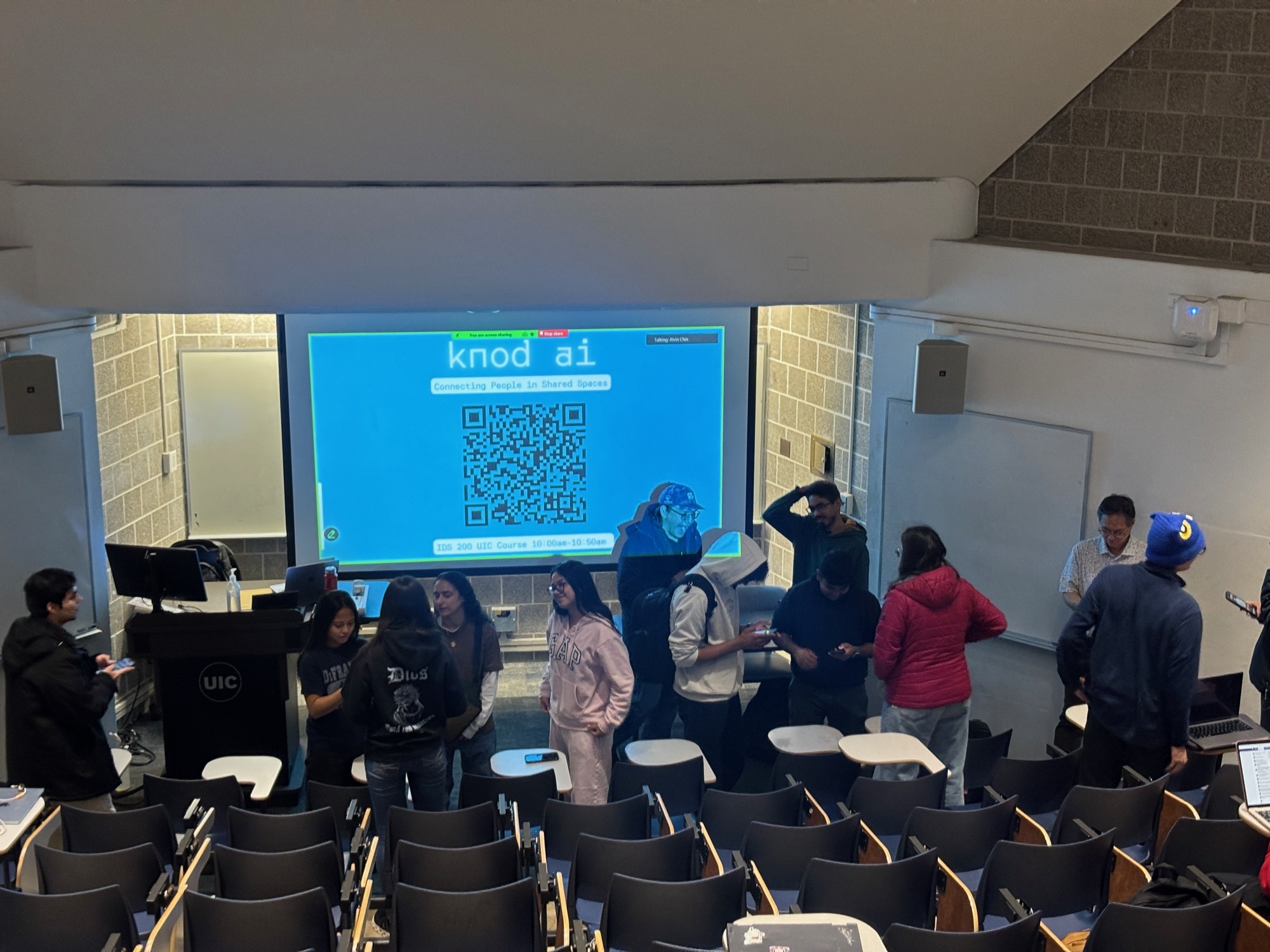 A UIC lecture hall with students mingling and the Knod screen for IDS 200